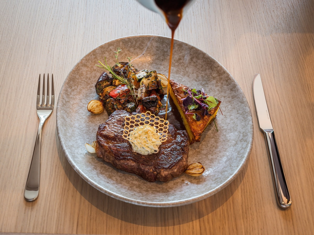 Saftig gebratenes Steak auf einem grau meliertem Teller, serviert mit Grillgemüse