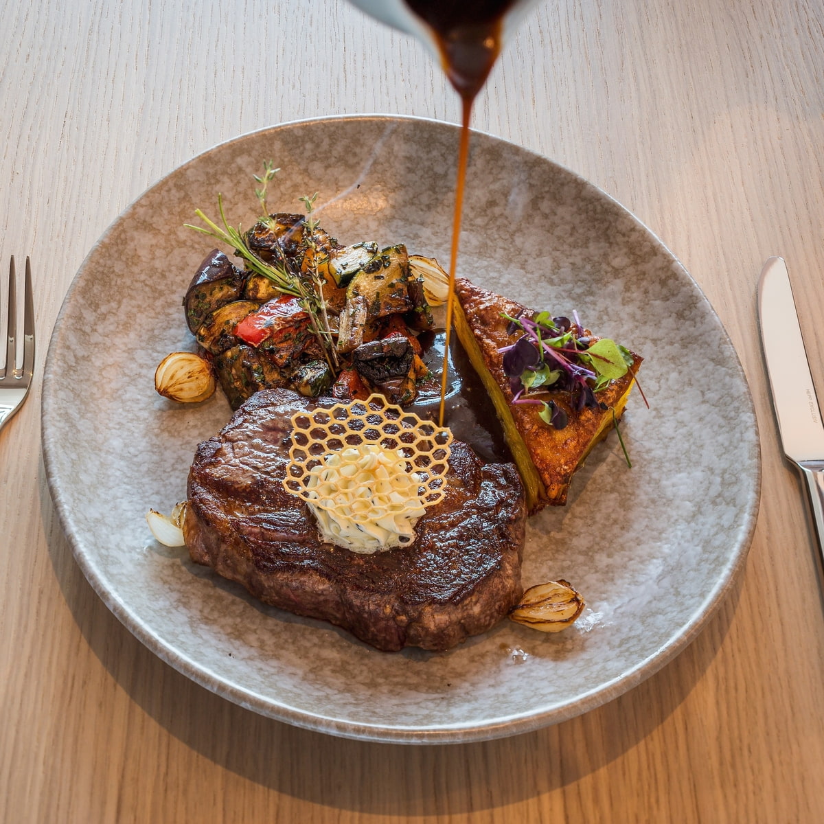 Saftig gebratenes Steak auf einem grau meliertem Teller, serviert mit Grillgemüse Saftig gebratenes Steak auf einem grau meliertem Teller, serviert mit Grillgemüse